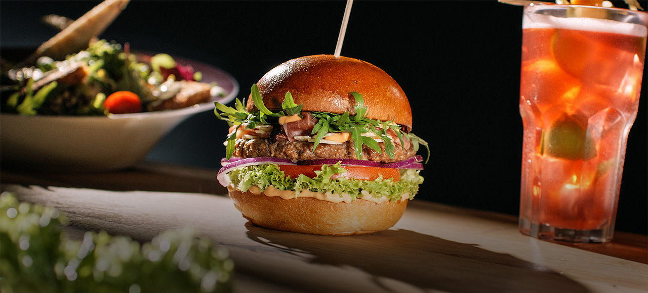 Saftiger Burger mit Salat und Cocktail im Hans im Glück – jetzt online bestellen und frisch genießen.