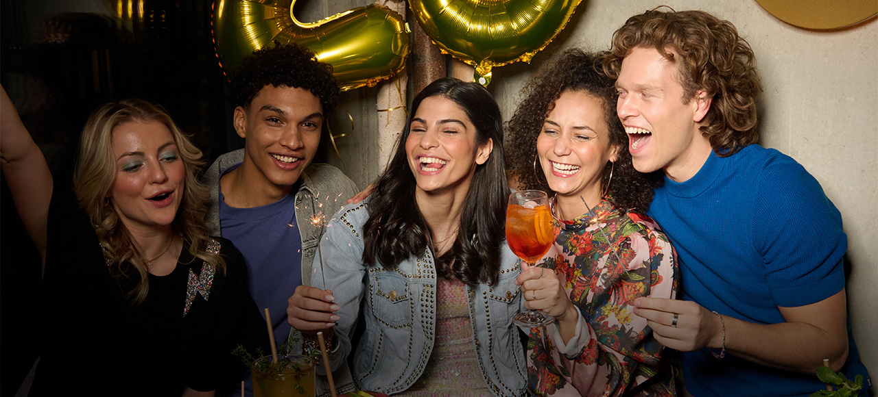 Junge Menschen feiern mit Cocktails in fröhlicher Runde – jetzt Tisch im Hans im Glück Restaurant online reservieren.